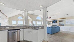 A spacious kitchen with a dishwasher, a large island, and a view to the living area. - Wink Shores | Oceanfront | Private Pool, Hot Tub, and Dog Friendly (Kill Devil Hills)