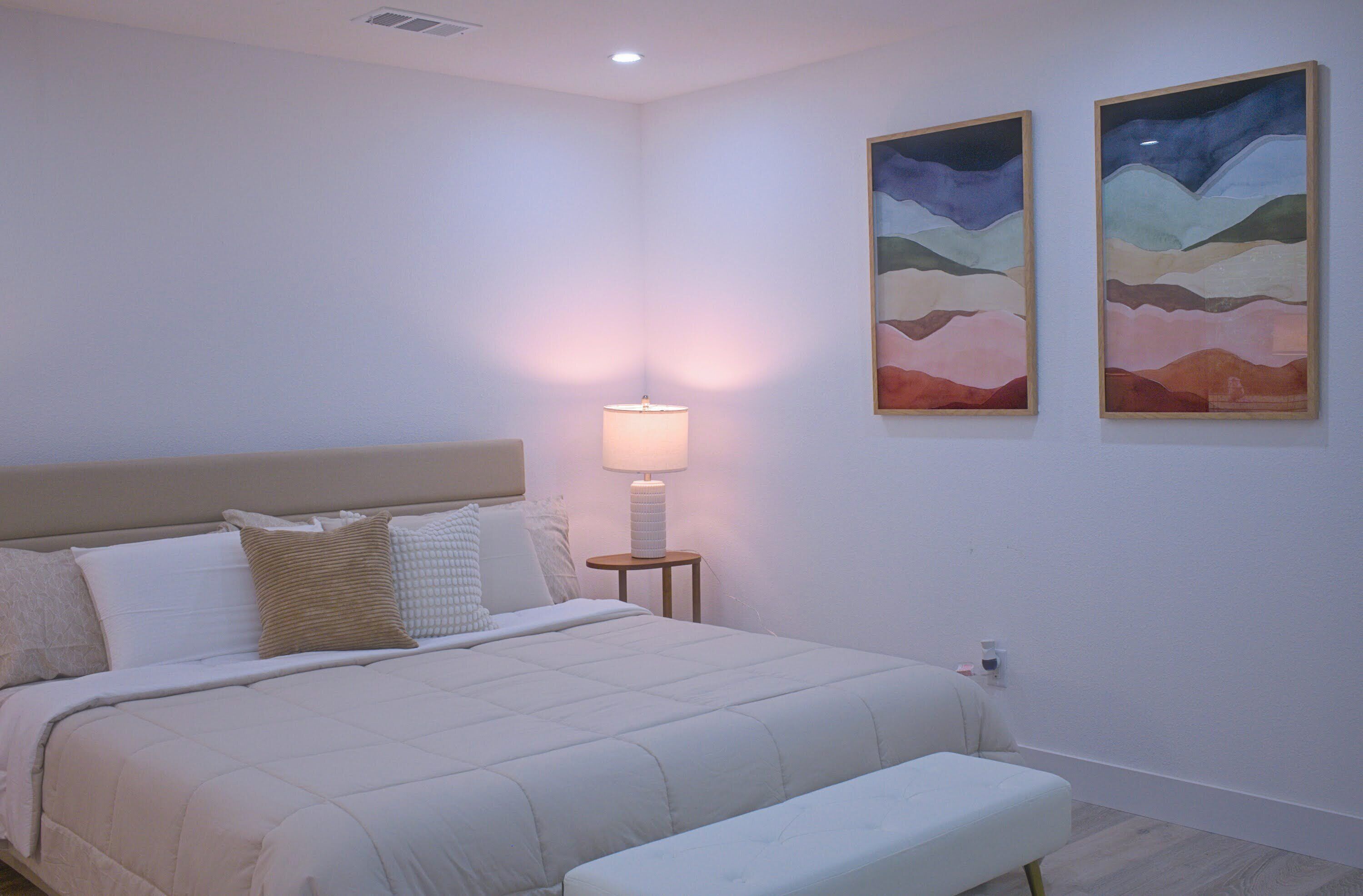 Une chambre à coucher avec un lit, une lampe de chevet et deux tableaux accrochés au mur.