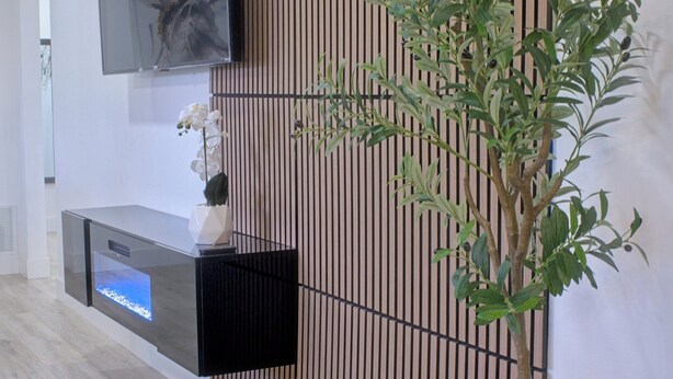 A modern interior with a wooden slat wall, a flat-screen TV mounted above a black console, and a potted plant. - Cozy Arlington Home • Minutes to AT&T & Globe Life (Arlington)