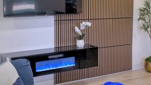 A modern living room with a flat-screen TV mounted on the wall, a ceiling fan, and a decorative plant. - Cozy Arlington Home • Minutes to AT&T & Globe Life (Arlington)