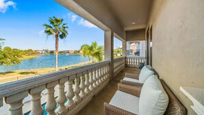 Ein Balkon mit Korbmöbeln und Blick auf einen See und Palmen.