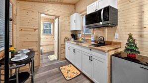 A compact kitchen with wooden walls, a microwave, a sink, and a refrigerator. - Tiny Retreat-Huge Covered Deck,Hot Tub,Lake Access (Sevierville)