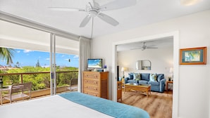 A bedroom with a large bed, a ceiling fan, a TV, and a view of the outdoors. - Lovely 2bd in Kihei, paradise awaits! (Kihei)