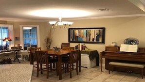 Un comedor con una mesa y sillas de madera, una araña, un piano y un cuadro abstracto enmarcado en la pared.