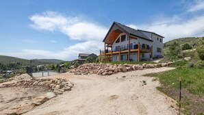 Ein modernes, zweistöckiges Haus mit einem großen Balkon, einer Schotterauffahrt und einer hügeligen Landschaft im Hintergrund.