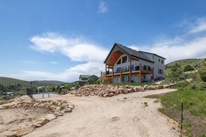 Ein modernes, zweistöckiges Haus mit einem großen Balkon, einer Schotterauffahrt und einer hügeligen Landschaft im Hintergrund.
