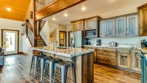 A spacious kitchen with a large island, wooden cabinets, and a staircase leading to an upper level. - Lazy Bear Lodge with Private Hot tub and Kayak (Garden City)