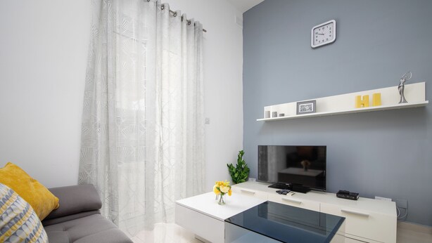 Una sala de estar moderna con un sofá, una mesa de centro, un televisor y una estantería con objetos decorativos.