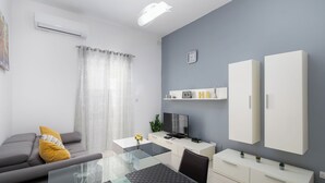 Una sala de estar moderna con una mesa de comedor de vidrio, sofá gris y armarios blancos.