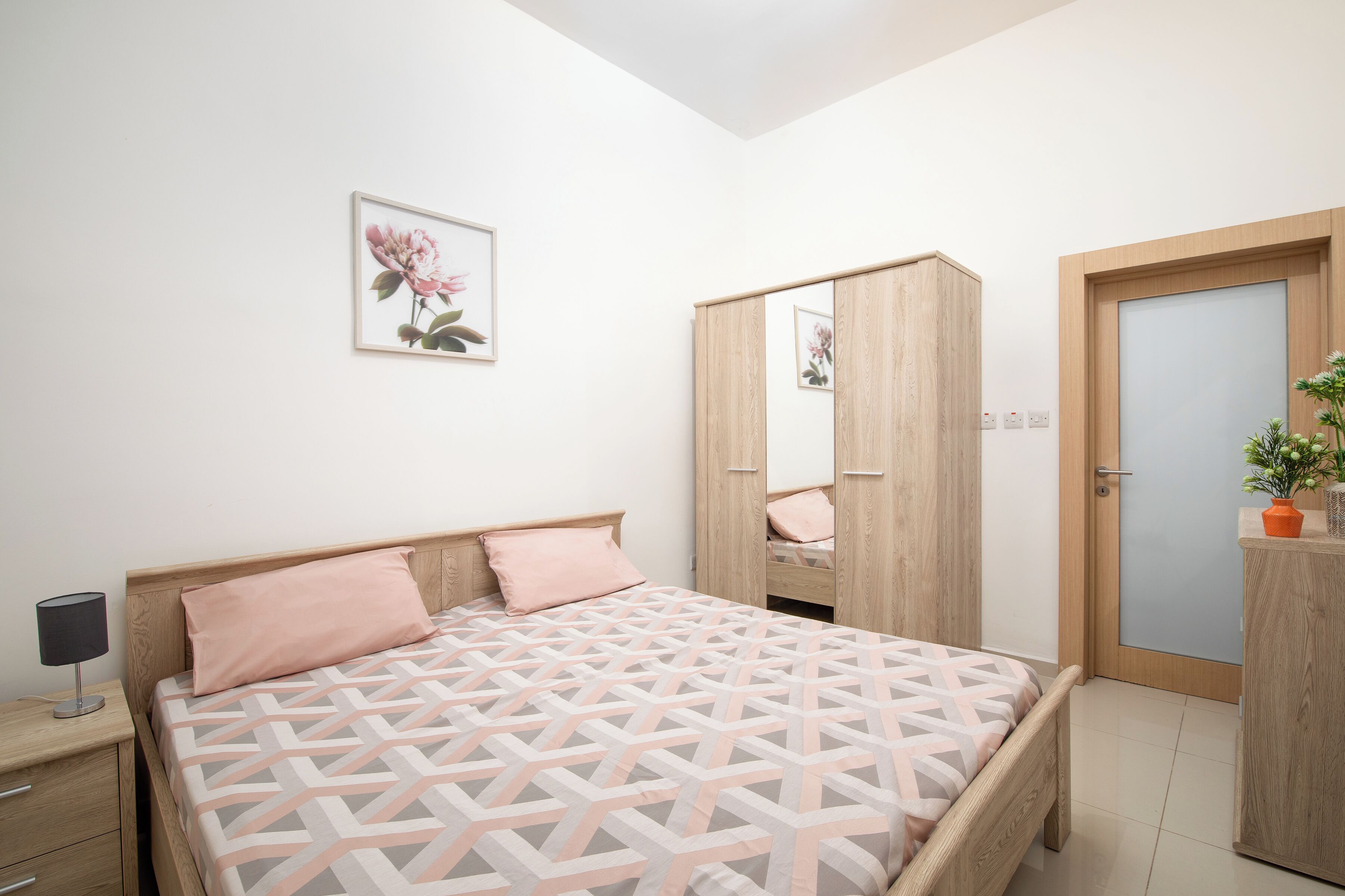 Une chambre à coucher avec un lit, une table de chevet, une commode, un miroir et une porte.