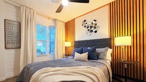 Un dormitorio con una cama grande, un ventilador de techo, un aplique de pared y una ventana con cortinas.