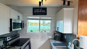 Una cocina moderna con un ventanal grande, electrodomésticos de acero inoxidable y un cartel que dice 'Kitchen the heart of the home'.