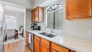 Une cuisine moderne avec des meubles en bois, un plan de travail blanc et une fenêtre équipée de stores.