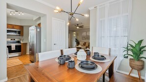Un coin repas avec une table en bois dressée pour quatre personnes, un lustre moderne et une vue sur la cuisine.