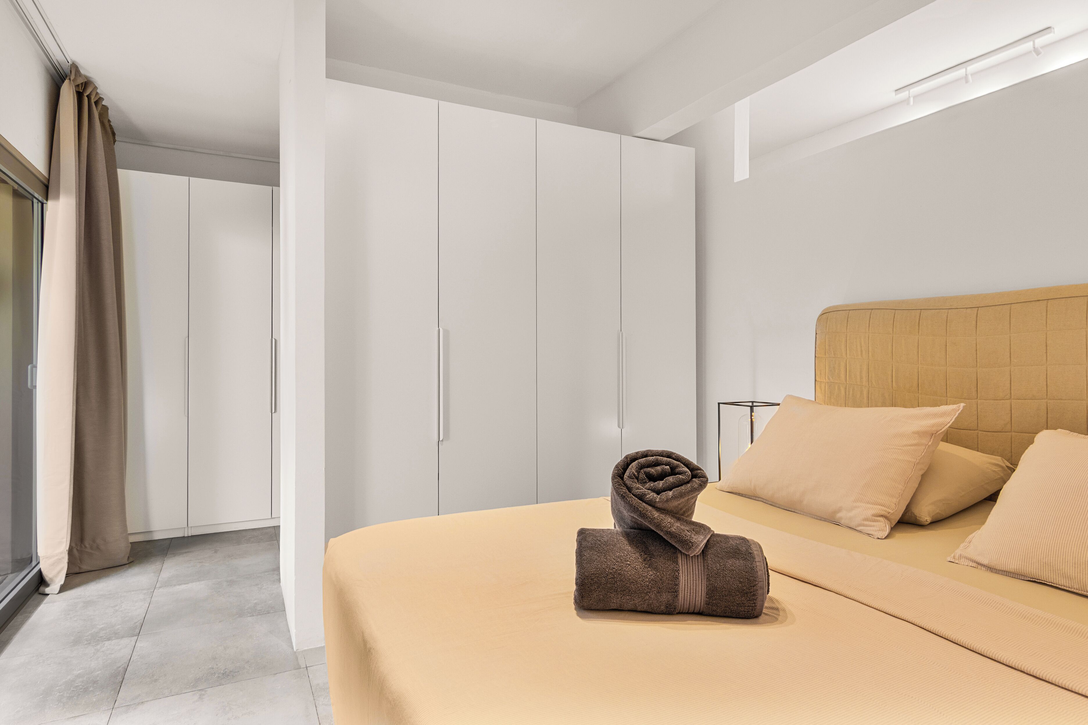 Ein modernes Hotelzimmer mit einem großen Bett, beigefarbener Bettwäsche, einem Holz-Kopfteil und einem Schrank mit Schiebetüren.