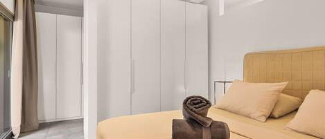 Ein modernes Hotelzimmer mit einem großen Bett, beigefarbener Bettwäsche, einem Holz-Kopfteil und einem Schrank mit Schiebetüren.