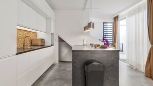 Eine moderne Küche mit weißen Schränken, einer Marmorinsel, Pendelleuchten und Blick ins Wohnzimmer.