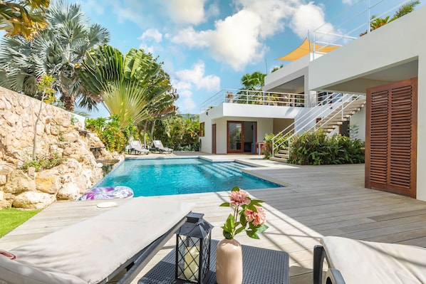 A modern poolside area with a stone wall, lounge chairs, and a wooden deck.