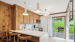 A modern kitchen with wooden cabinets, a central island with bar stools, and a large sliding glass door leading to a patio. - Mtn House w/ Hot Tub & Sauna @ Scribners, Sleeps 4 (Tannersville)