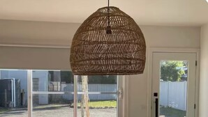 A room with a large window, a wicker pendant light, a black bench with circular cutouts, and a potted plant. - Premium Halls Gap Holiday Home - Firepit and Local Wine (Halls Gap)