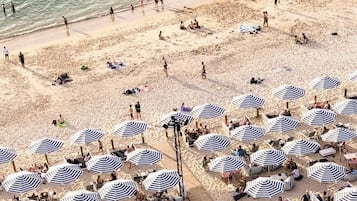 A beach with multiple striped umbrellas and beach chairs, indicating a beach club setting.