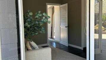 An open sliding glass door leading to a living area with a sofa, a potted plant, and a dark floor.