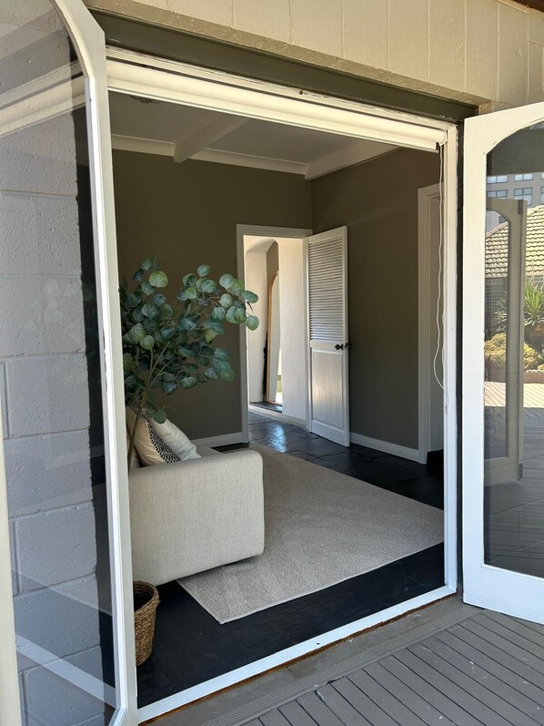 An open sliding glass door leading to a living area with a sofa, a potted plant, and a dark floor.
