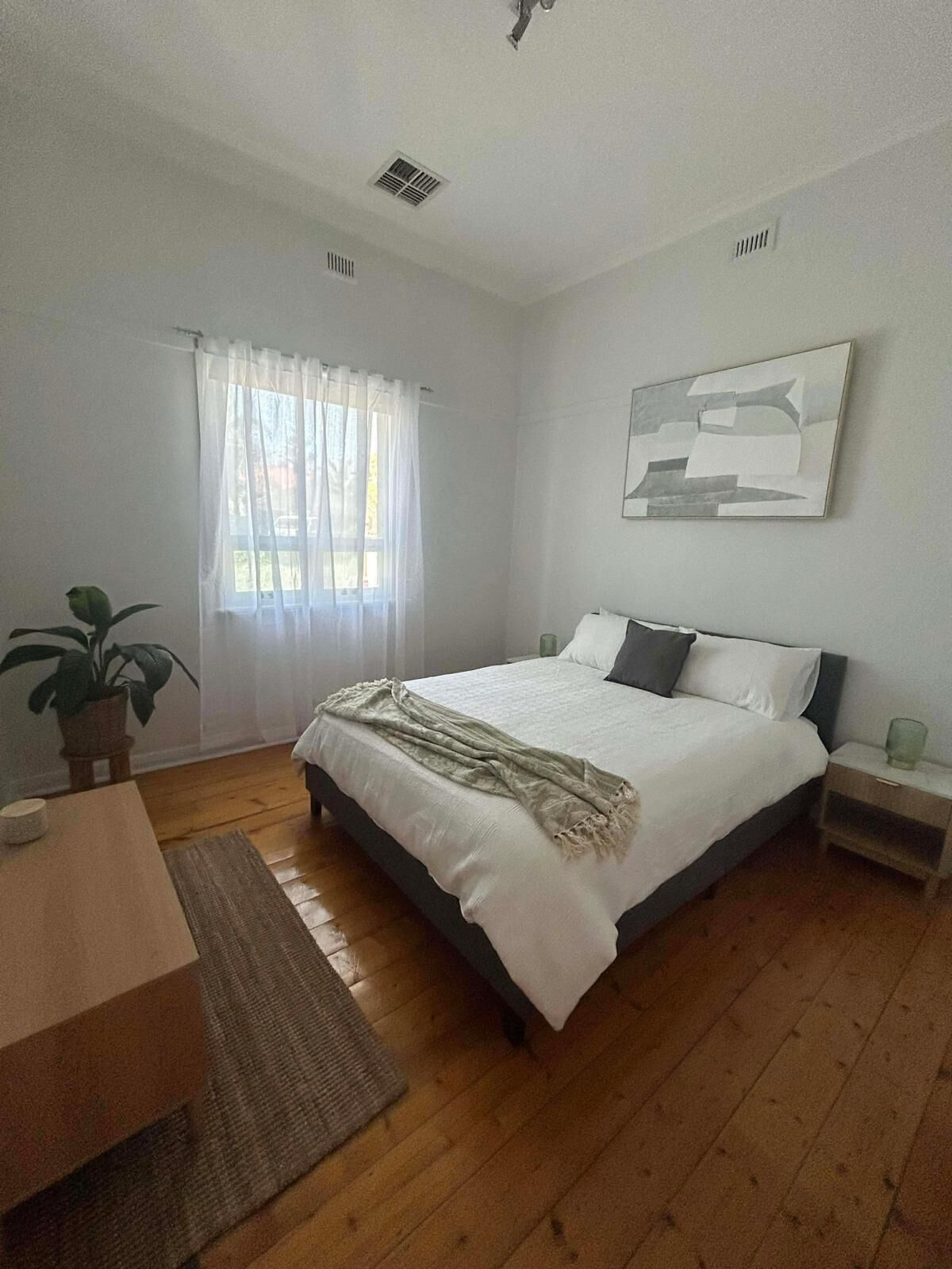 Quarto com cama, mesa de cabeceira, planta em vaso e um quadro na parede.