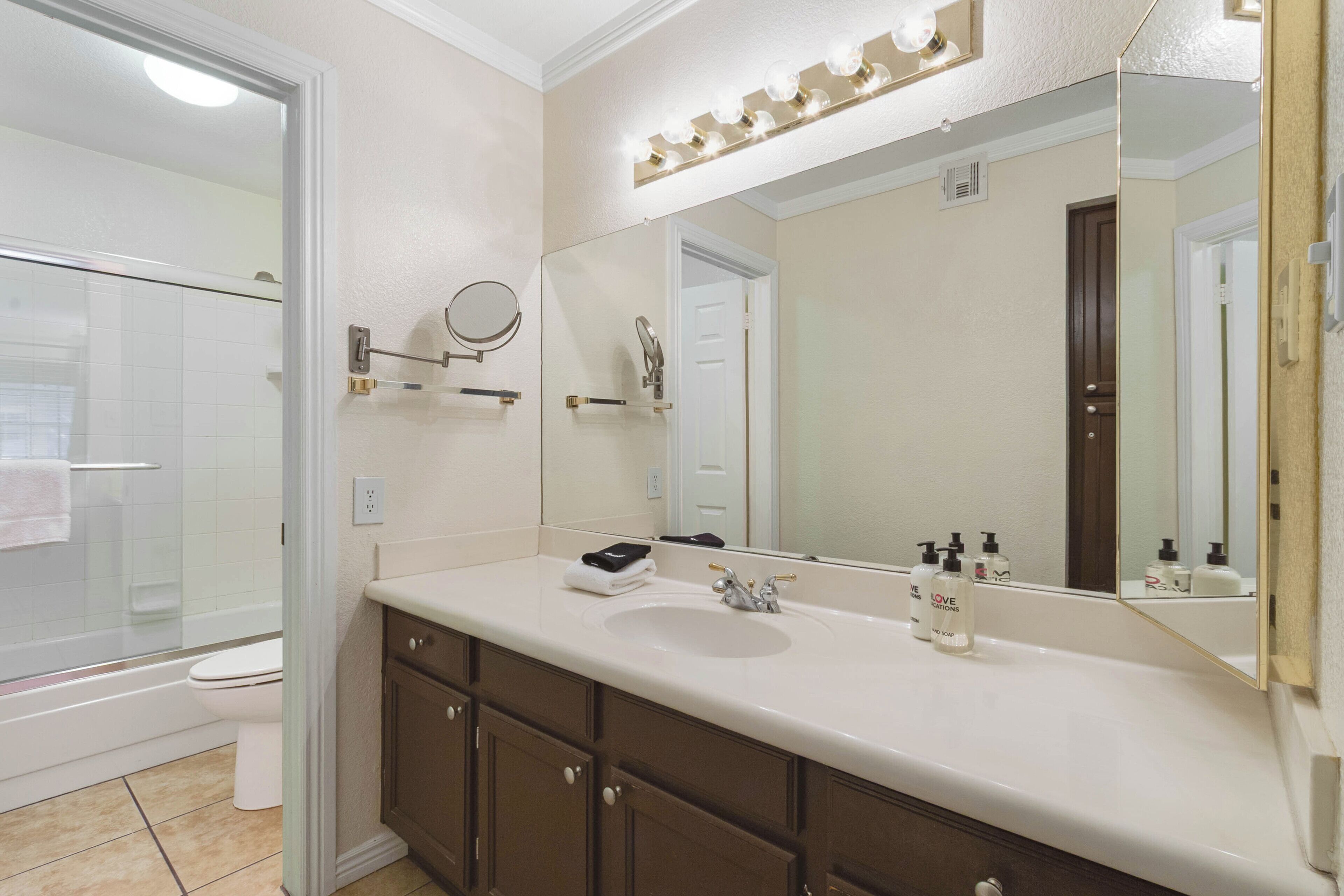 A bathroom with a white sink, dark brown cabinets, a large mirror, and a glass shower enclosure.