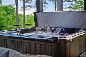 A hot tub with water jets, surrounded by a wooden deck and trees. - Mini Marshmallow Cabin - Cozy & Romantic GetAway (Broken Bow)