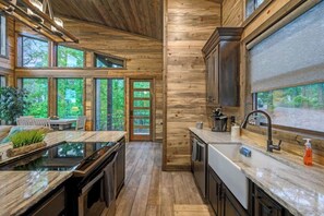 A modern kitchen with wooden walls, large windows, and a view of greenery. - Mini Marshmallow Cabin - Cozy & Romantic GetAway (Broken Bow)