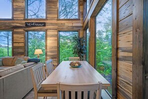 A wooden interior with a dining table, chairs, a sofa, and a 'Welcome' sign. - Mini Marshmallow Cabin - Cozy & Romantic GetAway (Broken Bow)
