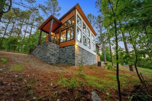 A modern house with a stone base, large windows, and a wooden roof. - Mini Marshmallow Cabin - Cozy & Romantic GetAway (Broken Bow)