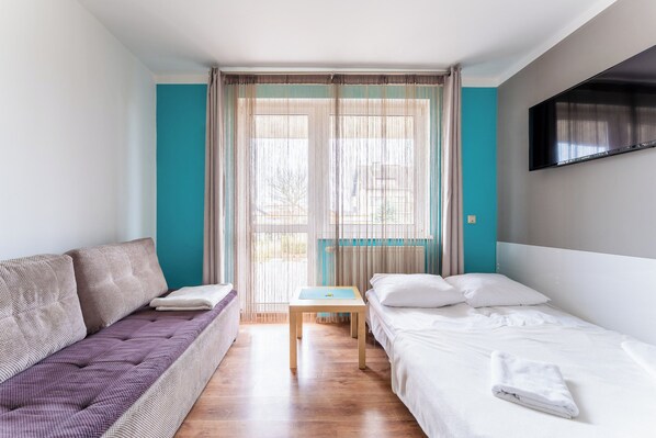 A modern hotel room with a sofa, a bed, a small table, and a TV. - Kołobrzeg Brylantowa Sea Studio #5 (Kołobrzeg)