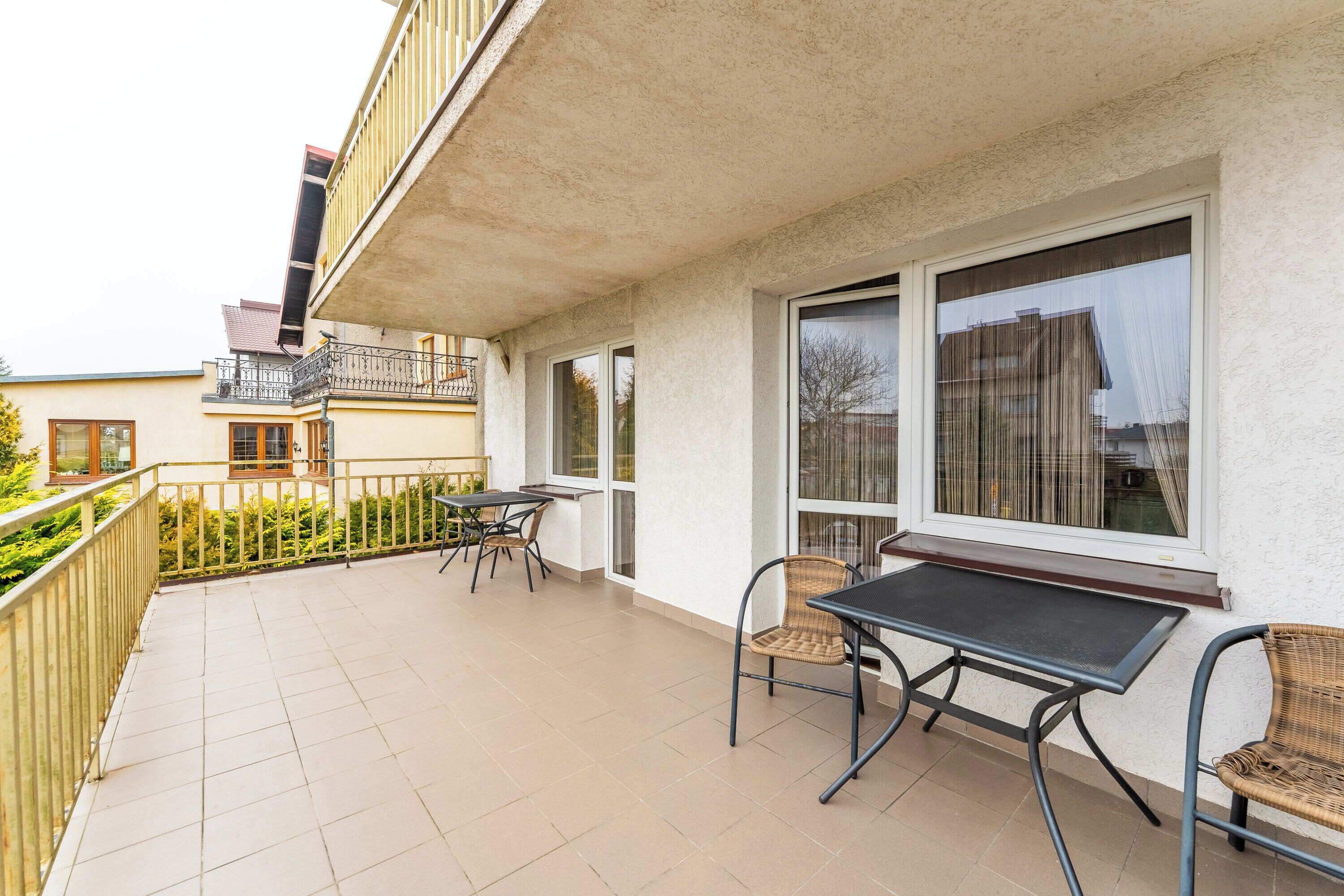 Een balkon met een tafel en stoelen, een leuning en uitzicht op omliggende gebouwen.