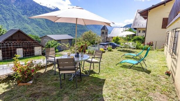 Un patio con mesa y sillas, un gran paraguas y montañas al fondo.