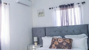 Ein Schlafzimmer mit Bett, Nachttisch, Klimaanlage und einem fenster mit Vorhängen.