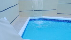 Ein Pool mit einer weißen Liege und einem Wasserspiel.