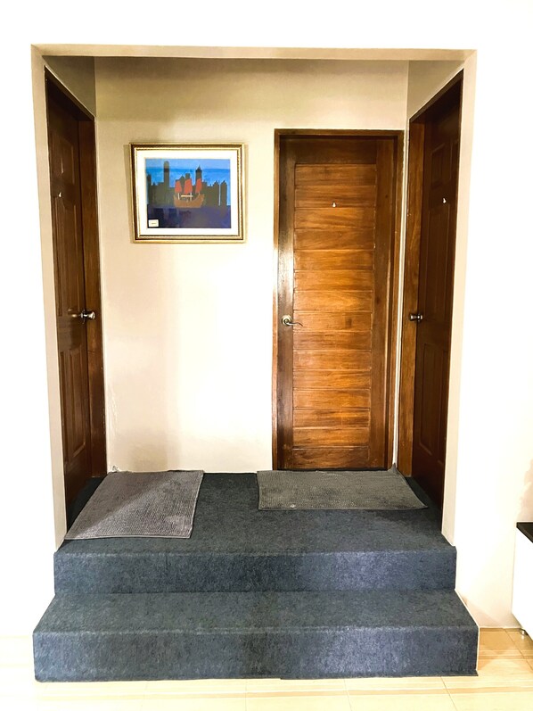Una habitación con puerta de madera, un cuadro enmarcado en la pared y una zona alfombrada con escalones que conducen a una puerta.