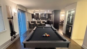 Una mesa de billar en una sala de estar moderna, con una cocina al fondo.