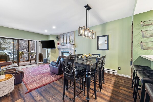 A spacious living room with a large window, a fireplace, and a dining area with a wooden table and chairs. - SunRiver Condo Close to BC & Vail - Pet Friendly (Avon)