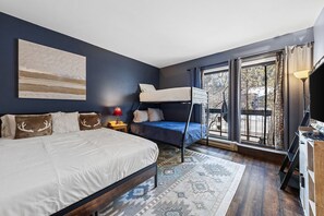 A bedroom with a large bed, a bunk bed, a TV, and a view through a glass door. - SunRiver Condo Close to BC & Vail - Pet Friendly (Avon)