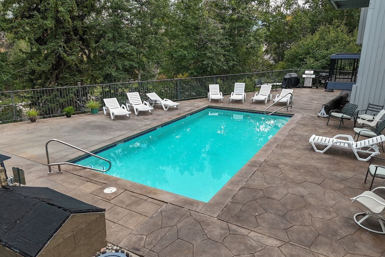 A rectangular swimming pool with a tiled deck, surrounded by white lounge chairs and potted plants.