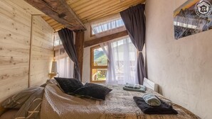 Un dormitorio acogedor con techo de madera, un ventanal con cortinas, una cama con colcha estampada y vistas a un paisaje montañoso.