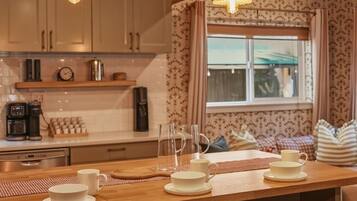 A kitchen with wooden bar stools, a coffee station, and a window with curtains.