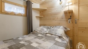 Een gezellige kamer met houten plafond, een bed met een quilt met patroon, een raam met gordijnen en wandlampen.