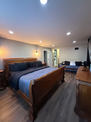 A bedroom with a wooden bed, a nightstand, a dresser, and a wall-mounted light fixture. - Luxe Home with Michelin Star Kitchen & King Beds (Bolingbrook)