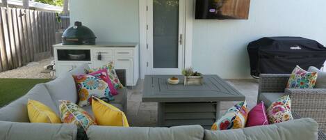 Un patio cubierto con sofá, mesa, parrilla y televisor montado en la pared.