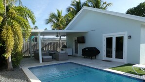 Un espace piscine extérieur moderne, doté d’un coin salon couvert, d’un barbecue et d’une petite terrasse.