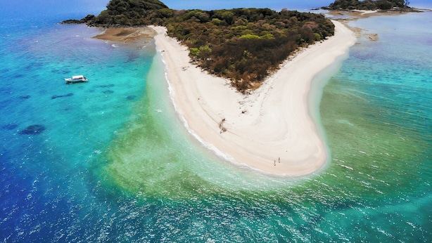 Luchtbeeld van een strand met helder turquoise water, een zandstrand en een boot in het water.